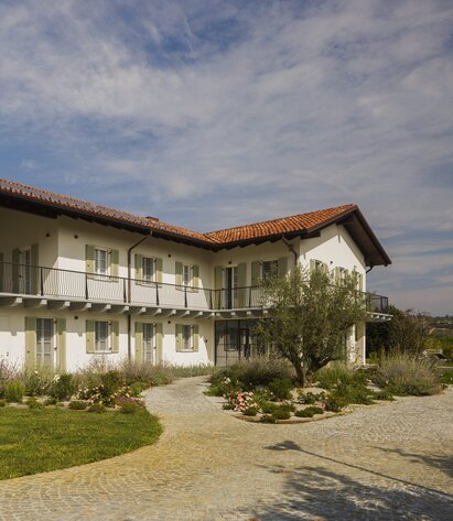 A two-storey house with a red tiled roof, painted white façade and light green shutters | © Alessandro Santi