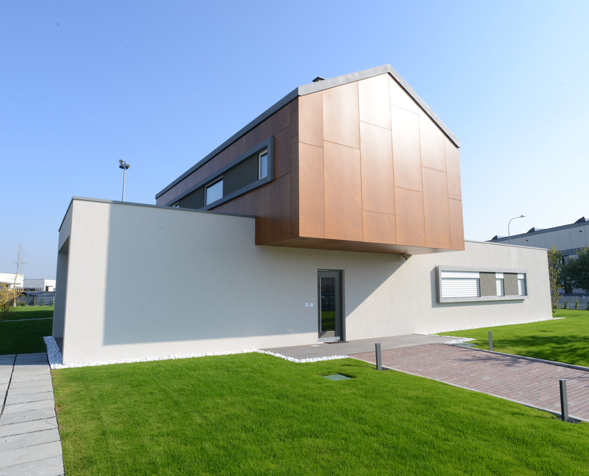 Una casa a due piani, con il piano superiore ruotato di 90° rispetto al piano inferiore. Il piano inferiore è intonacato e tinteggiato di bianco, il piano superiore è rivestito con pannelli di facciata ad effetto legno. | © Marco Baraldi