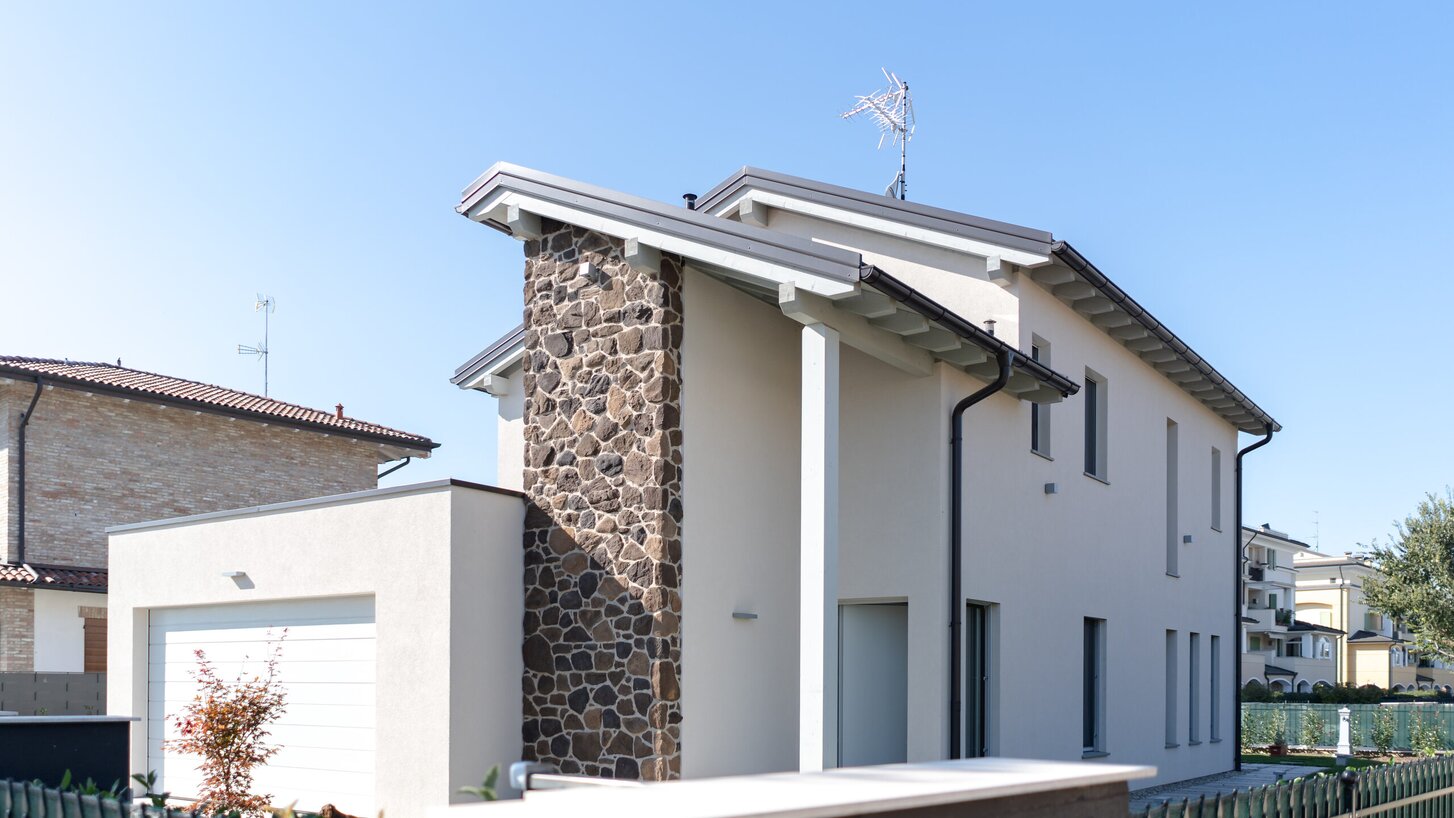 Una casa a due piani con pareti esterne bianche, una parte è rivestita in pietra