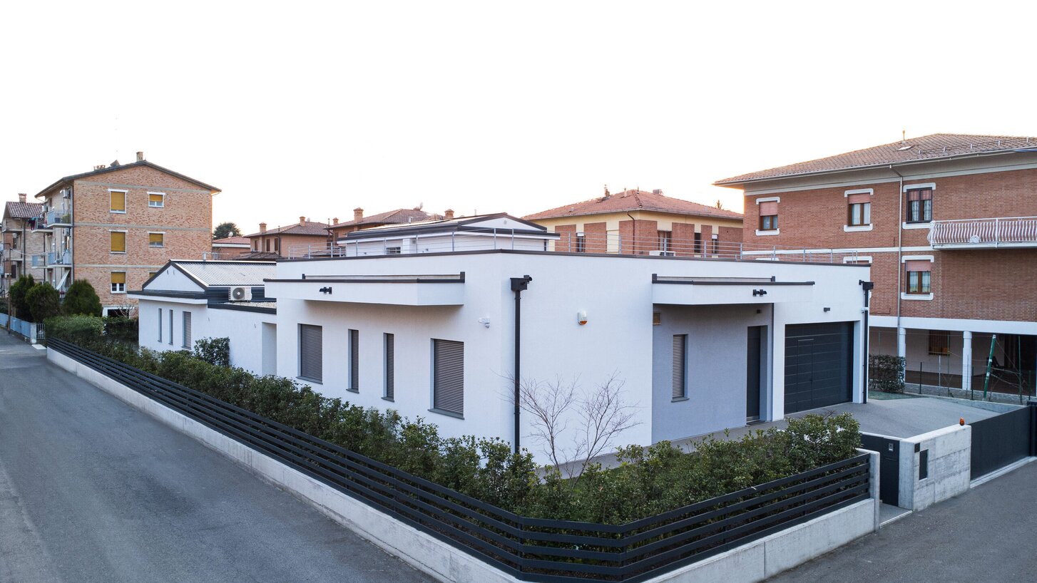 Un edificio a un piano con facciata bianca circondato da una siepe in una zona residenziale