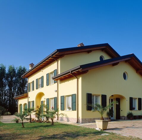 Una casa a due piani con la facciata dipinta di giallo e persiane verdi | © LignoAlp - Damiani-Holz&KO