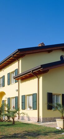 Una casa a due piani con la facciata dipinta di giallo e persiane verdi | © LignoAlp - Damiani-Holz&KO
