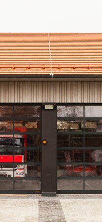 Einfahrt einer Feuerwehrhalle mit Außenschalung aus Holz und Einfahrtstoren aus Glas. | © Regina Sedlmayer