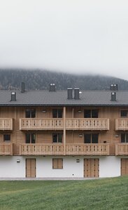 Ein dreistöckiges Gebäude mit einer verputzten Fasssade im Erdgeschoss und Fensterläden aus Holz, die zwei Obergeschosse und die Balkone sind aus naturbelassenem Holz | © Davide Perbellini