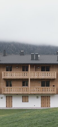 Edificio a tre piani con facciata intonacata al piano terra e scuri in legno, i due piani superiori e i balconi sono in legno non trattato | © Davide Perbellini