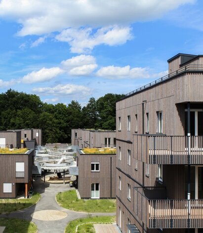 A large residential complex with three and four-storey buildings with façades made of pre-greyed wooden slats and a curved pergola as an entrance | © Regina Sedlmayer