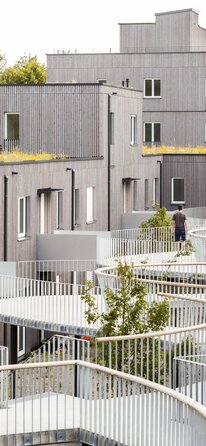 A large residential complex with three and four-storey buildings with façades made of pre-greyed wooden slats and a curved pergola as an entrance | © Regina Sedlmayer