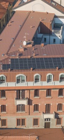 Ein historisches Gebäude, auf dem durch eine Aufstockung eine zusätzliche Ebene enstanden ist. Die Aufstockung ist außen mit kupferfarbenem Blech verkleidet, auf dem Dach sind Photovoltaikmodule angebracht