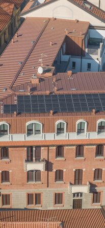 Un edificio storico a cui è stato aggiunto un piano aggiuntivo. L'ampliamento è rivestito esternamente con lamiera color rame e sul tetto sono installati moduli fotovoltaici.