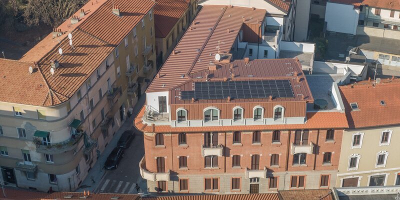 Un edificio storico a cui è stato aggiunto un piano aggiuntivo. L'ampliamento è rivestito esternamente con lamiera color rame e sul tetto sono installati moduli fotovoltaici.
