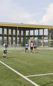 Ein Fußballfeld mit Spielern, im Hintergrund ein großes Gebäude mit vielen Fenstern und einem goldig glänzenden Dach | © Michele Nastasi