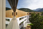 Ein Schulgebäude, auf den drei verputzten Untergeschossen steht ein vierter Stock mit einer vertikal laufenden Verkleidung aus Lärchenholz | © Samuel Holzner