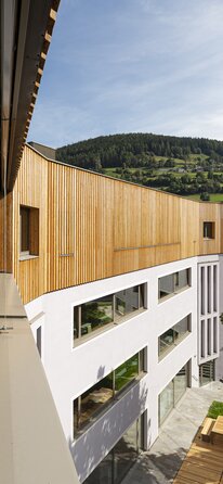 Ein Schulgebäude, auf den drei verputzten Untergeschossen steht ein vierter Stock mit einer vertikal laufenden Verkleidung aus Lärchenholz | © Samuel Holzner