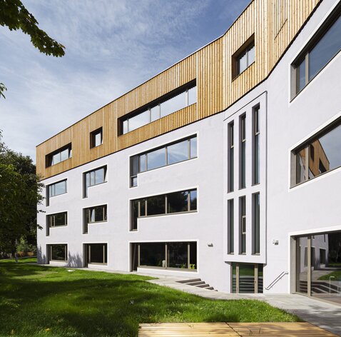 Ein Schulgebäude, auf den drei verputzten Untergeschossen steht ein vierter Stock mit einer Verkleidung aus Lärchenholz | © Samuel Holzner