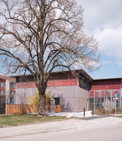 Fassade einer Schule in Holzbauweise mit vorvergrauter Fassadenschalung und roter Fassadenbahn | © Florian Holzherr