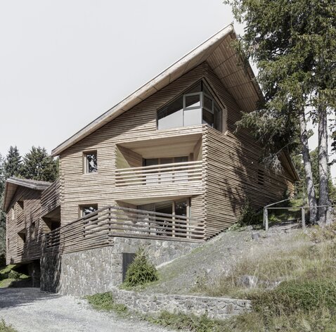 Ein Gebäude mit einem Sockel aus Naturstein und einer Fassadenverkleidung aus geviertelten Baumstämmen | © Gustav Willeit