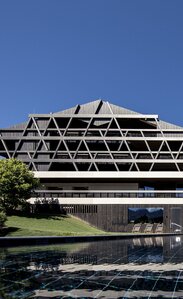 Ein großes Gebäude mit einer Fassade aus dunklem Holz, im Vordergrund ein Freischwimmbad | © Florian Andergassen