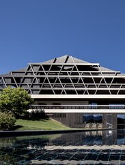 A large building with a façade of dark wood, in the foreground an outdoor swimming pool | © Florian Andergassen