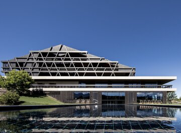 Ein großes Gebäude mit einer Fassade aus dunklem Holz, im Vordergrund ein Freischwimmbad | © Florian Andergassen
