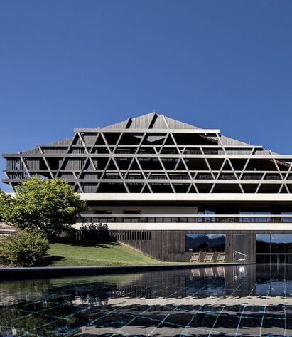 Un grande edificio con una facciata in legno scuro, in primo piano una piscina all'aperto | © Florian Andergassen