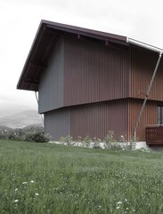 Ein großes Gebäude mit einer rotfarbigen Holzfassade, die durch vertikal verlaufende, dreieckige Leisten gegliedert ist, die auf der einen Seite gelb und auf der anderen Seite blau gestrichen sind | © Gustav Willeit