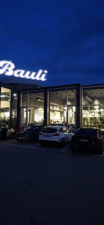 Eine Autobahnraststätte in der Nacht mit großen Glasflächen, auf dem Dach steht der Schriftzug "Bauli"
