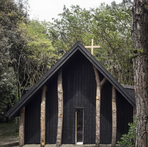 Eine kleine Kapelle aus dunklem Holz umgeben von Bäumen | © Alessandra Chemollo