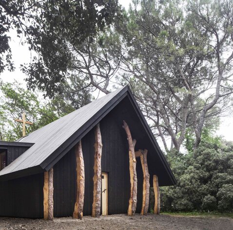 Una piccola cappella in legno scuro, circondata da alberi. | © Alessandra Chemollo
