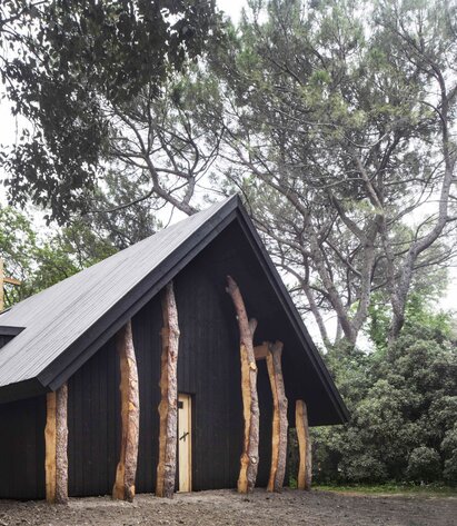 Una piccola cappella in legno scuro, circondata da alberi. | © Alessandra Chemollo