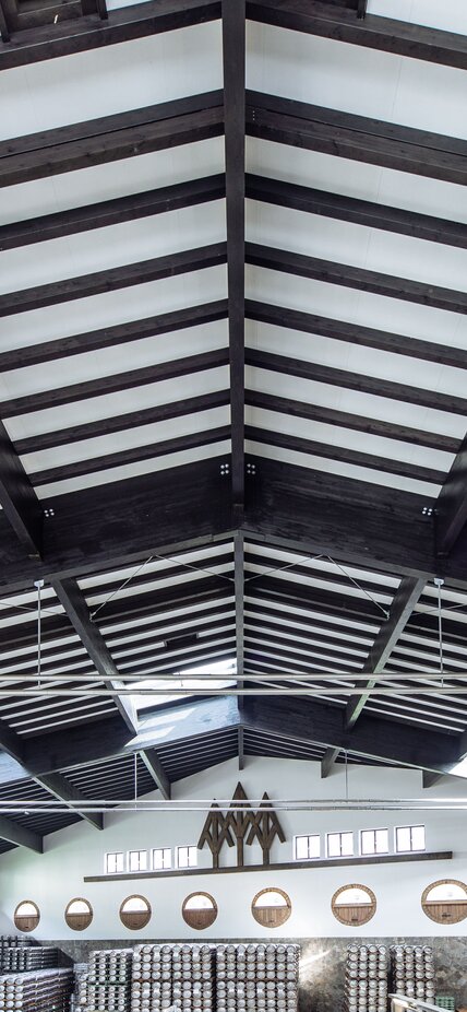 La struttura del tetto in legno di un grande capannone di produzione con travi in legno lamellare verniciate di scuro | © Benjamin Pfitscher