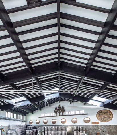 La struttura del tetto in legno di un grande capannone di produzione con travi in legno lamellare verniciate di scuro | © Benjamin Pfitscher