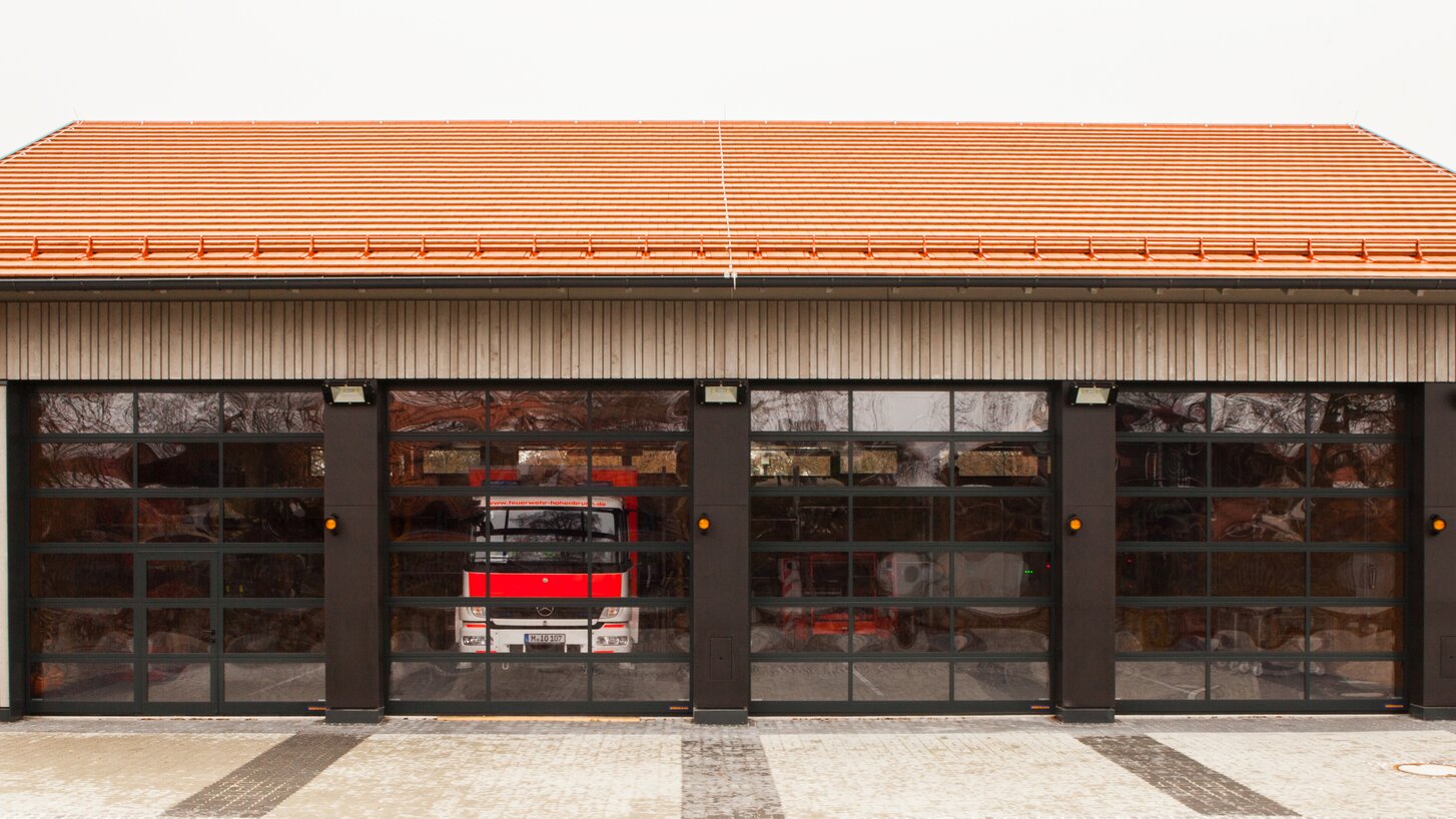 Einfahrt einer Feuerwehrhalle mit Außenschalung aus Holz und Einfahrtstoren aus Glas. | © Regina Sedlmayer
