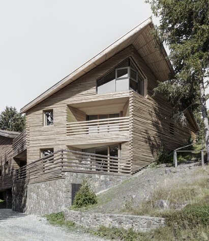 Ein Gebäude mit einem Sockel aus Naturstein und einer Fassadenverkleidung aus geviertelten Baumstämmen | © Gustav Willeit