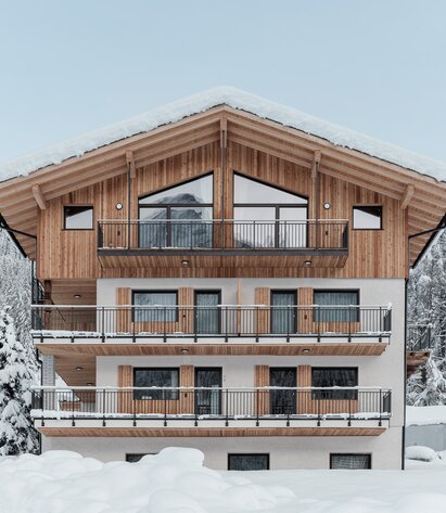 Un edificio circondato dalla neve; un nuovo piano con rivestimento esterno in legno si erge su tre piani intonacati | © Davide Perbellini