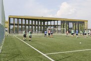 Ein Fußballfeld mit Spielern, im Hintergrund ein großes Gebäude mit vielen Fenstern und einem goldig glänzenden Dach | © Michele Nastasi