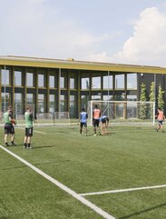 A football field with players, in the background a large building with many windows and a shiny golden roof | © Michele Nastasi