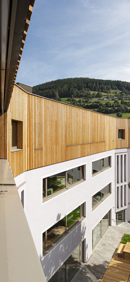 Edificio scolastico, ai tre piani seminterrati intonacati si aggiunge un quarto piano con rivestimenti in legno di larice. | © Samuel Holzner