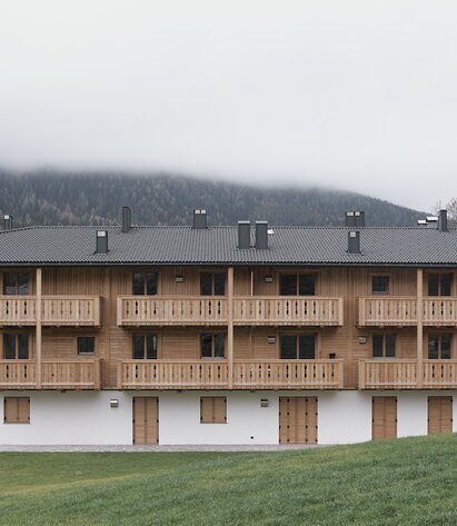 A three-storey building with a plastered façade on the ground floor and wooden shutters, the two upper floors and the balconies are made of natural wood | © Davide Perbellini