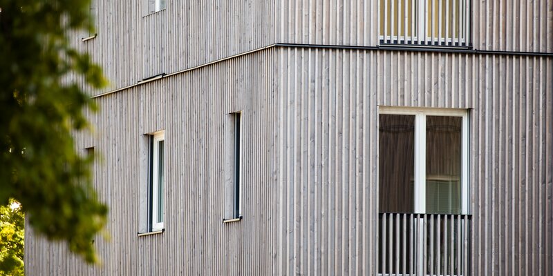 La facciata di un edificio con rivestimento di facciata con listelli in legno impregnati color grigio | © Regina Sedlmayer