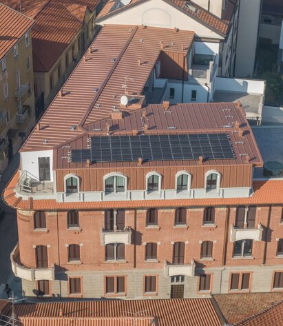 Ein historisches Gebäude, auf dem durch eine Aufstockung eine zusätzliche Ebene enstanden ist. Die Aufstockung ist außen mit kupferfarbenem Blech verkleidet, auf dem Dach sind Photovoltaikmodule angebracht