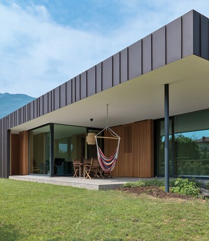 Una casa a un piano con ampie superfici vetrate, rivestimento in legno delle pareti e grande sporgenza del tetto piano | © Matteo Piazza
