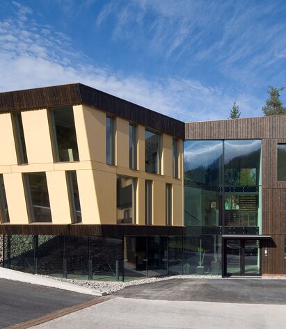Ein modernes Gebäude mit großen Fensterflächen und einer Verkleidung aus schwarzen Brettern und gelb lackierten Platten