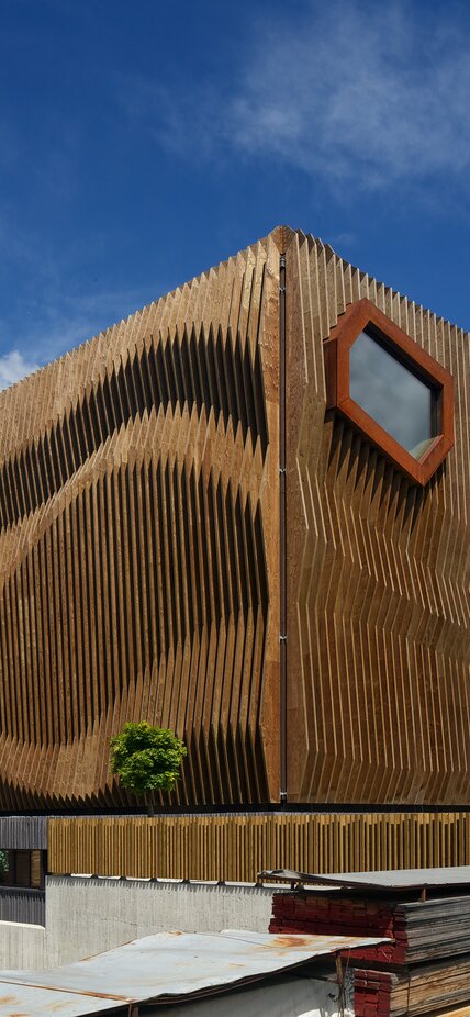 Un edificio a forma di cubo con una facciata di elementi in legno allineati verticalmente che creano visivamente un'onda. | © Günther Richard Wett